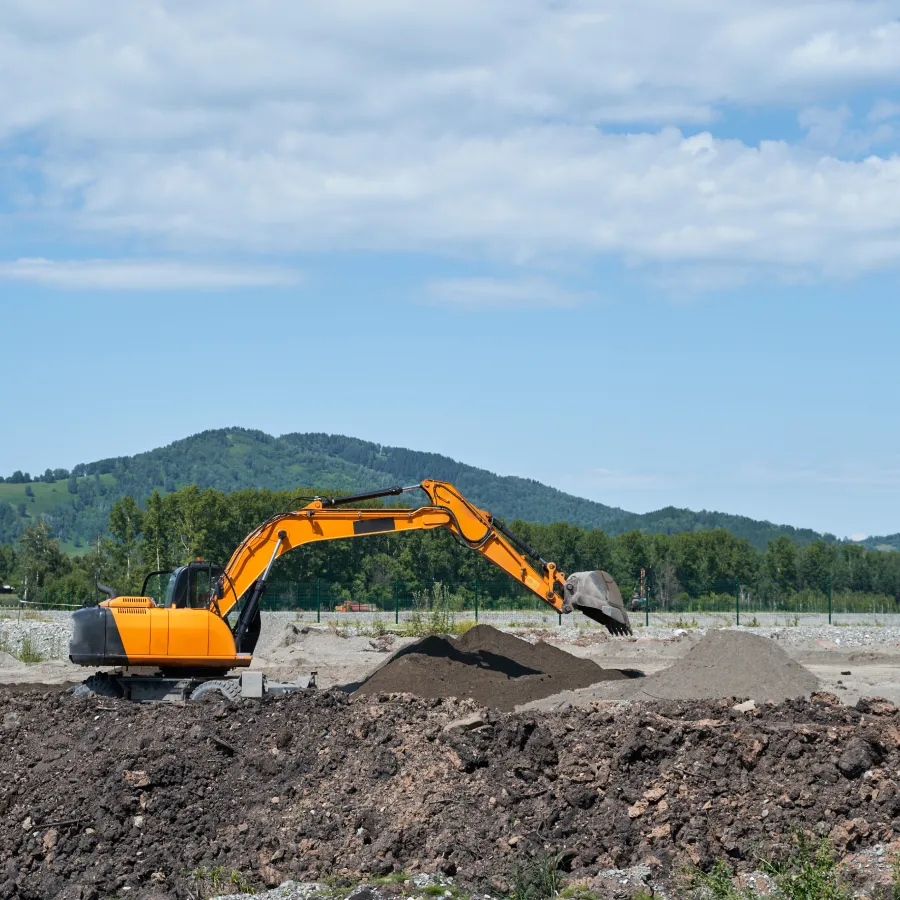 Yellow excavator in action on construction site with dirt pile and scenic mountain view.